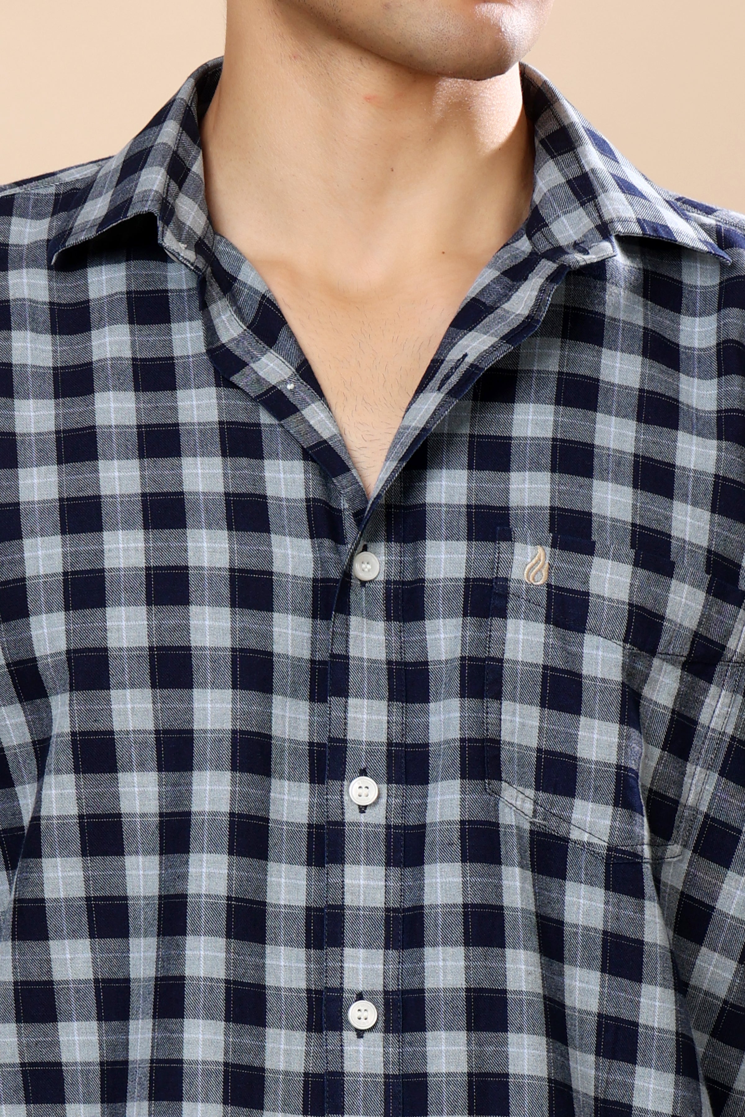 A close-up of a man wearing a navy blue and gray checkered button-down shirt, showing the collar, chest pocket, and front buttons.