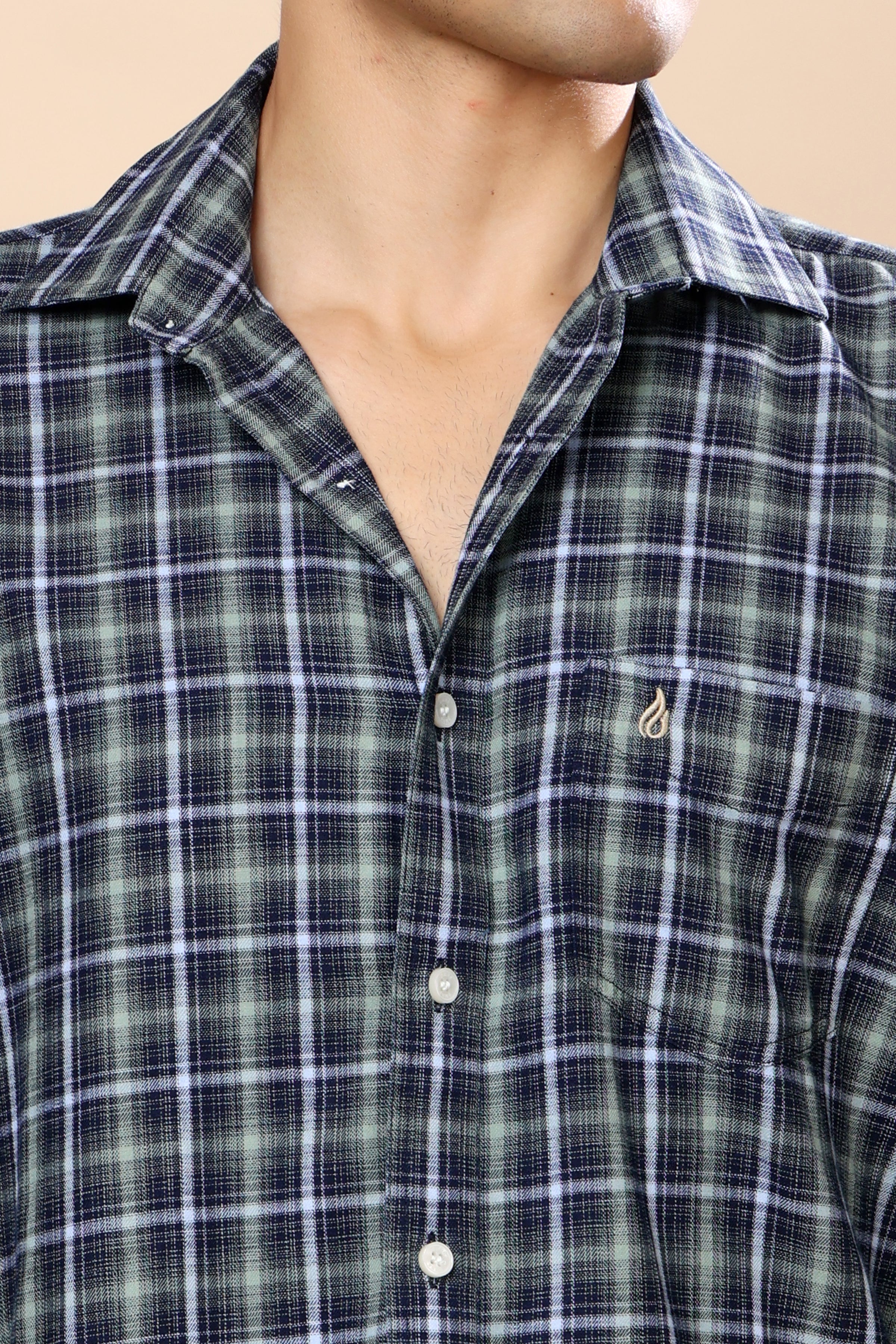 Close-up of a man wearing a green and navy plaid button-down shirt with a small embroidered logo on the chest pocket.