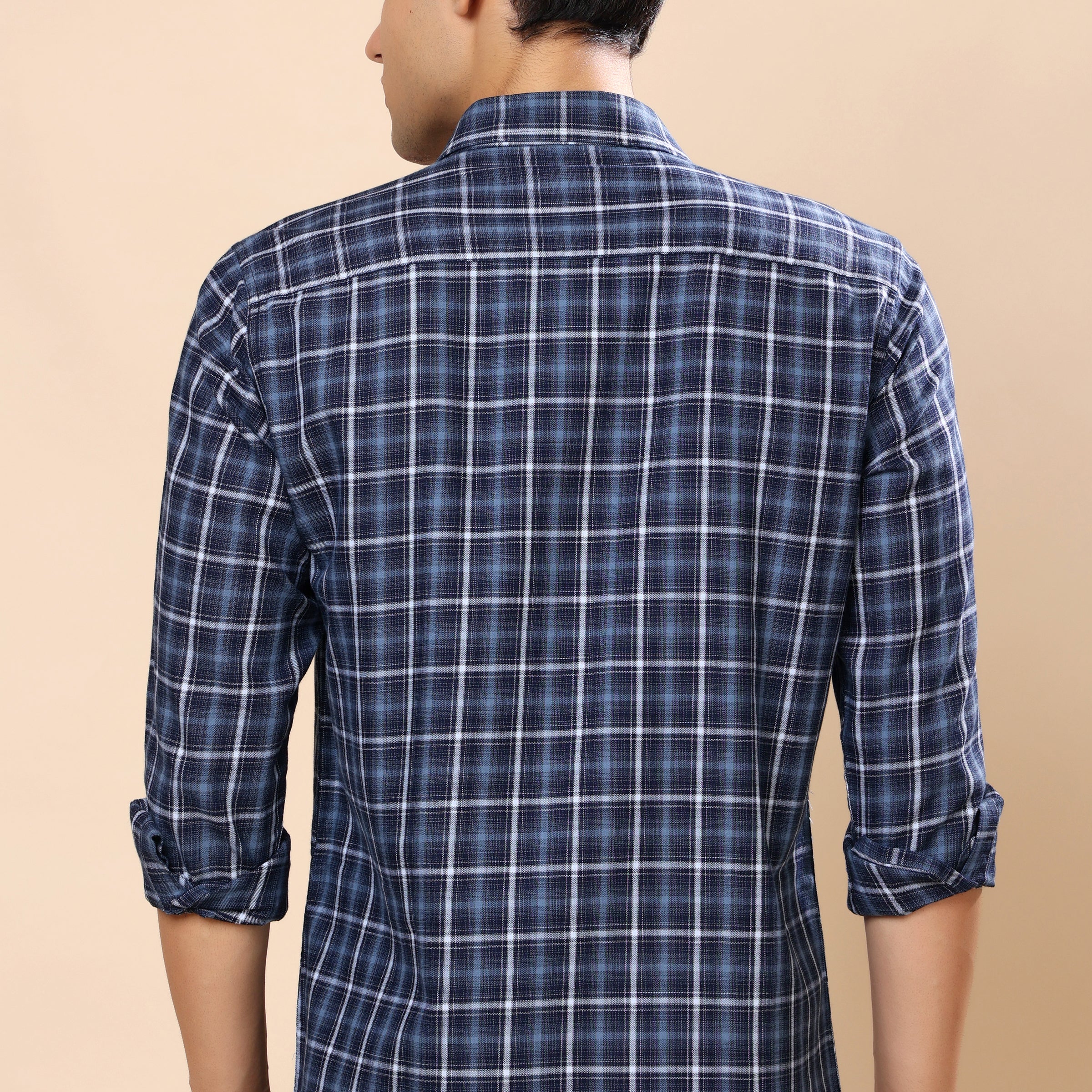 A man viewed from the back wearing a navy blue plaid long-sleeve shirt with white grid lines, set against a solid beige background.