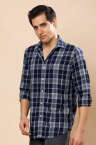 A man wearing a navy blue and gray plaid long-sleeve button-down shirt, standing against a solid beige background.