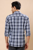 A man viewed from the back wearing a navy blue and white plaid long-sleeve shirt with rolled-up sleeves, set against a solid beige background.