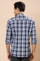 A man viewed from the back wearing a navy blue and white plaid long-sleeve shirt with rolled-up sleeves, set against a solid beige background.