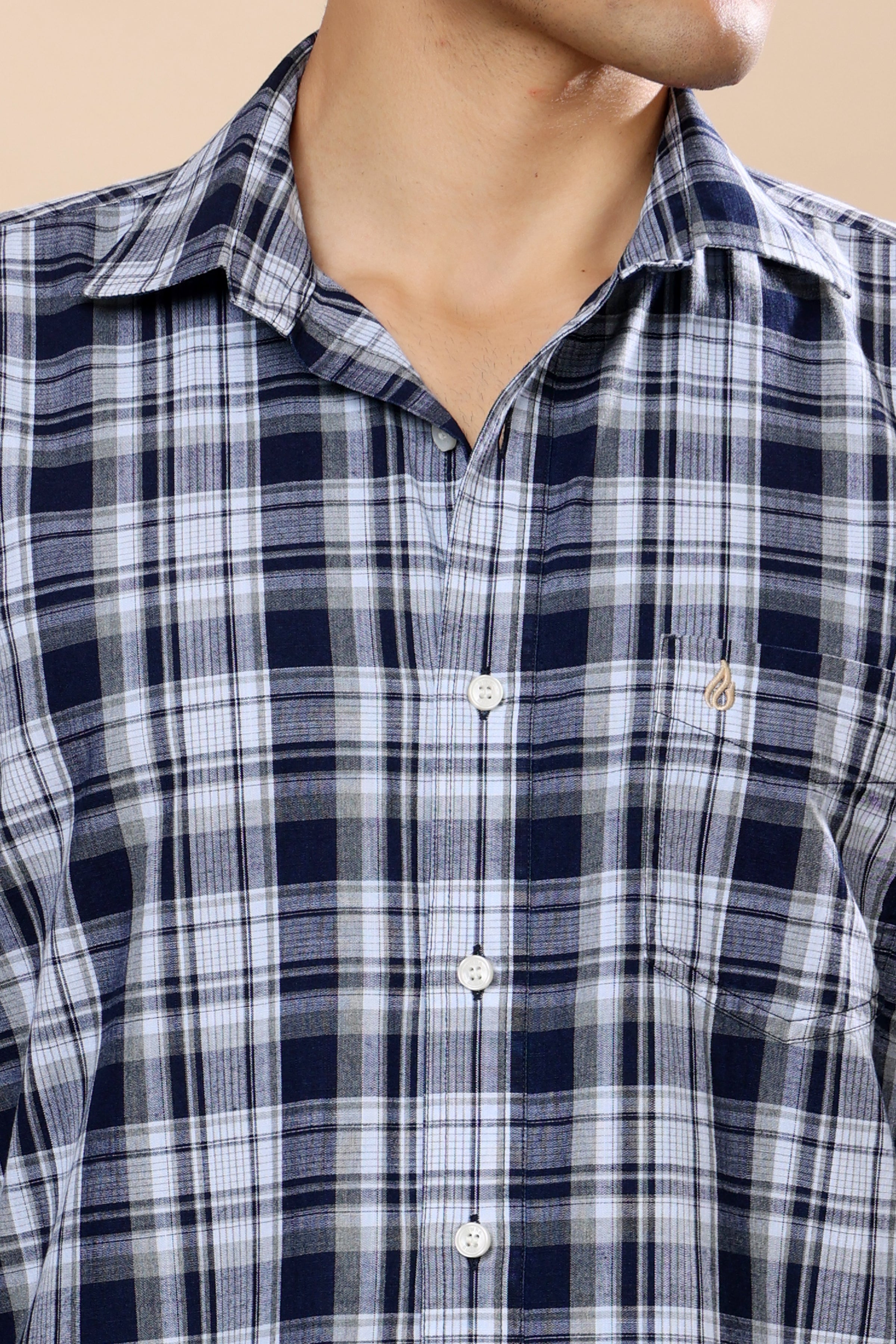 A close-up of a man wearing a navy blue, white, and gray plaid button-down shirt. The image shows the collar, chest pocket with a small embroidered logo, and front buttons.