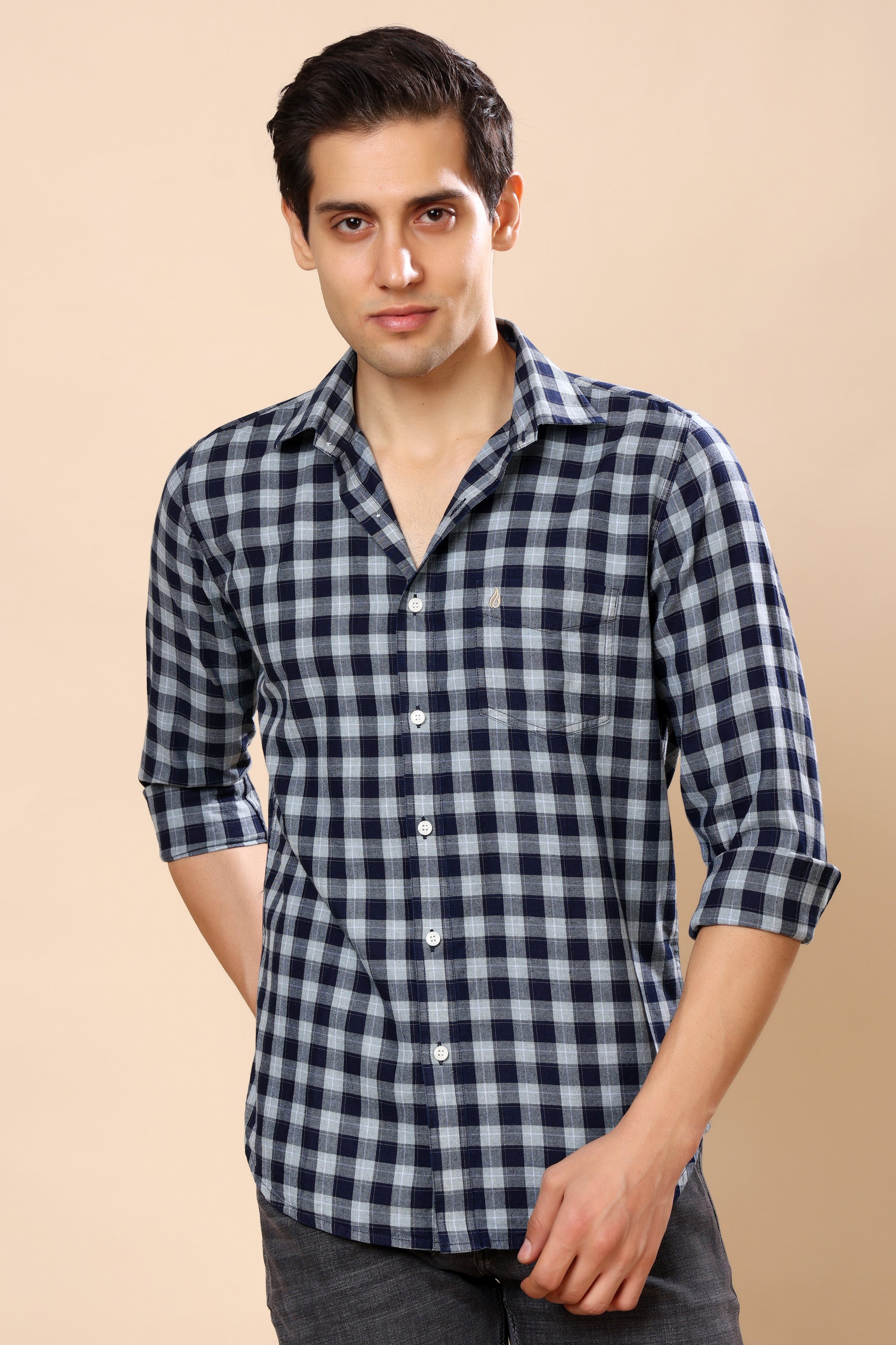 A man wearing a navy blue and white checkered long-sleeve button-up shirt, standing against a solid beige background.
