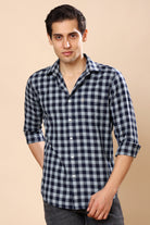 A man wearing a navy blue and white checkered long-sleeve button-up shirt, standing against a solid beige background.