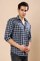A man wearing a black and white gingham check long-sleeve button-down shirt, paired with dark gray jeans, standing against a solid beige studio background.