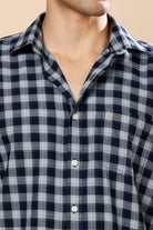 A close-up of a man wearing a navy blue and gray checkered button-down shirt, showing the collar, chest pocket, and front buttons.
