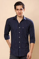 A man wearing a navy blue long-sleeve button-up shirt with thin white vertical stripes, standing against a solid beige background.