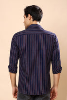 A man viewed from the back wearing a navy blue striped button-down shirt with thin red and white vertical lines, set against a solid beige background.