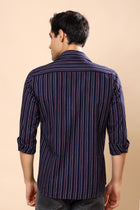 A man viewed from the back wearing a navy blue striped button-down shirt with thin red and white vertical lines, set against a solid beige background.