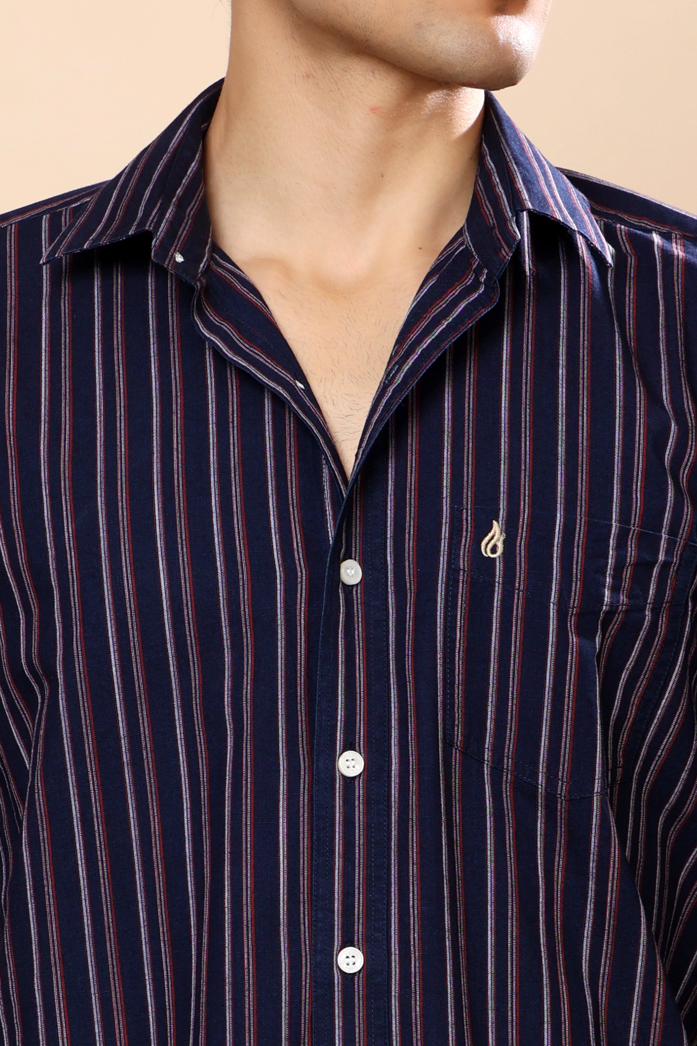 A close-up of a man wearing a navy blue button-down shirt with vertical red and white stripes, featuring a small embroidered logo on the chest pocket.