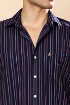 A close-up of a man wearing a navy blue button-down shirt with vertical red and white stripes, featuring a small embroidered logo on the chest pocket.
