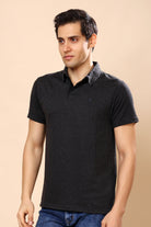 A man wearing a dark charcoal gray textured short-sleeve polo shirt with a small embroidered logo on the chest, paired with blue jeans, set against a solid beige background.