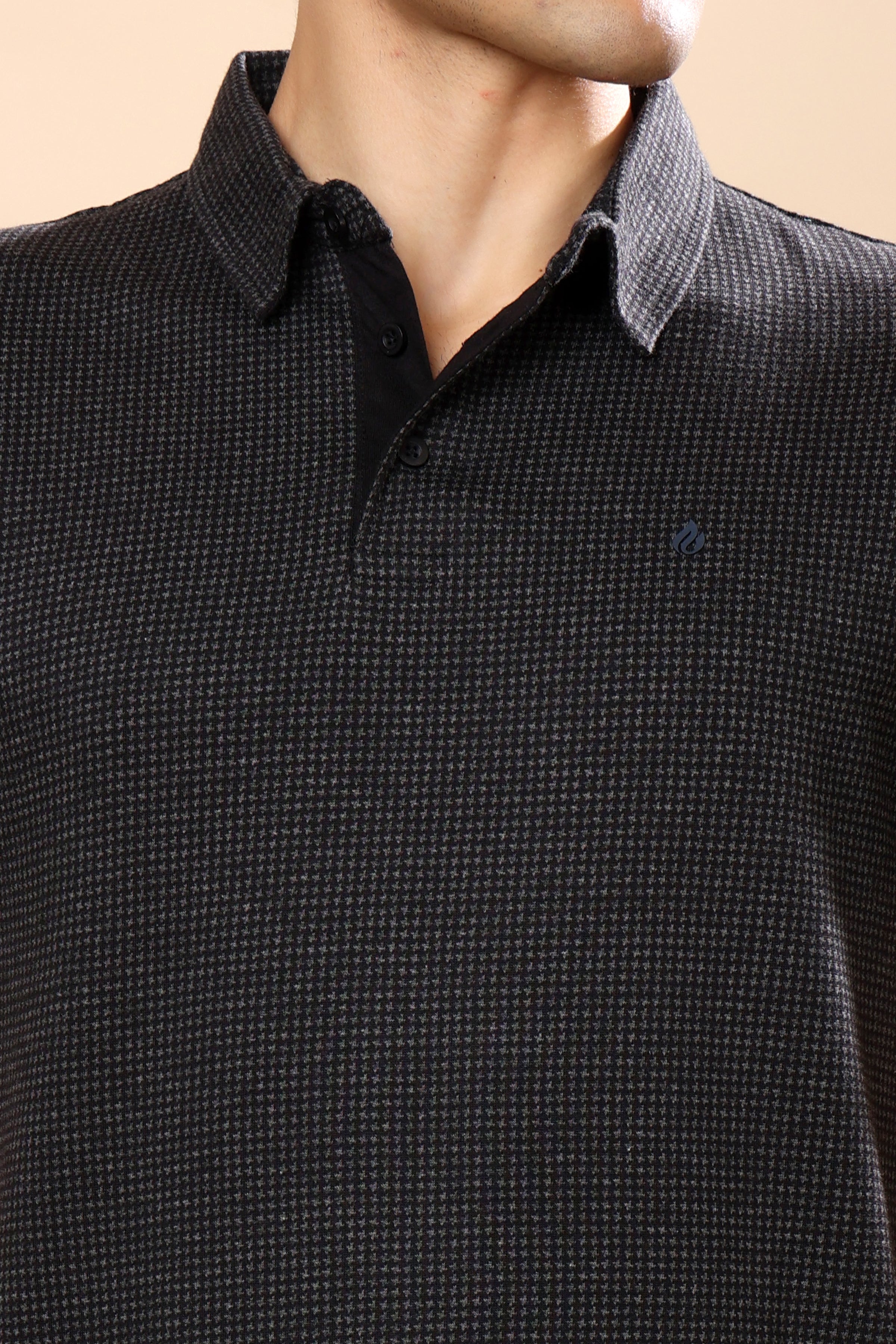 Close-up of a man wearing a dark charcoal gray and black micro-patterned polo shirt with a classic collar and a two-button placket.
