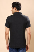 A man viewed from the back wearing a short-sleeve black textured polo shirt and blue jeans, set against a solid beige studio background.