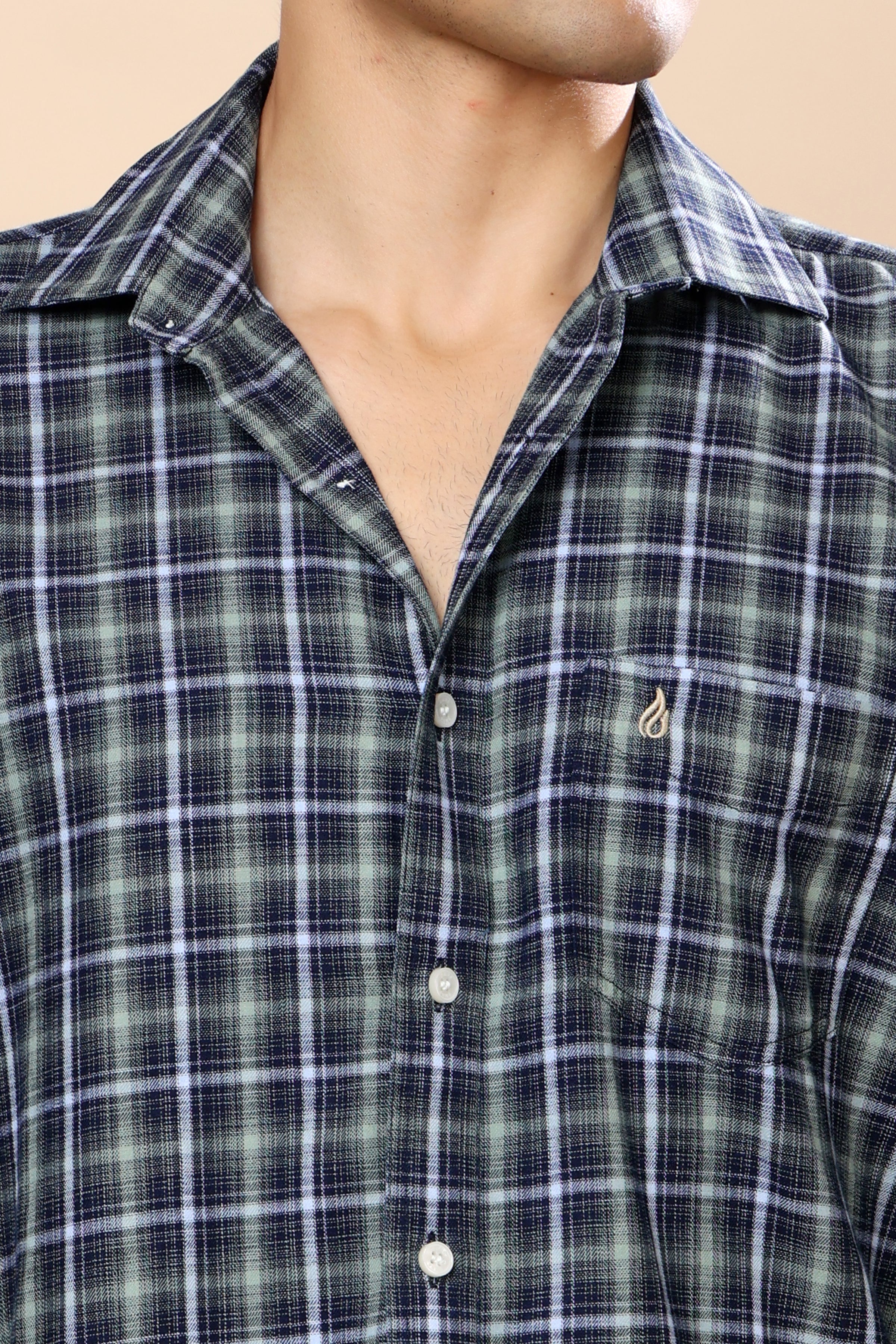 Close-up of a man wearing a green and navy plaid button-down shirt with a small embroidered logo on the chest pocket.