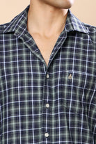 Close-up of a man wearing a green and navy plaid button-down shirt with a small embroidered logo on the chest pocket.