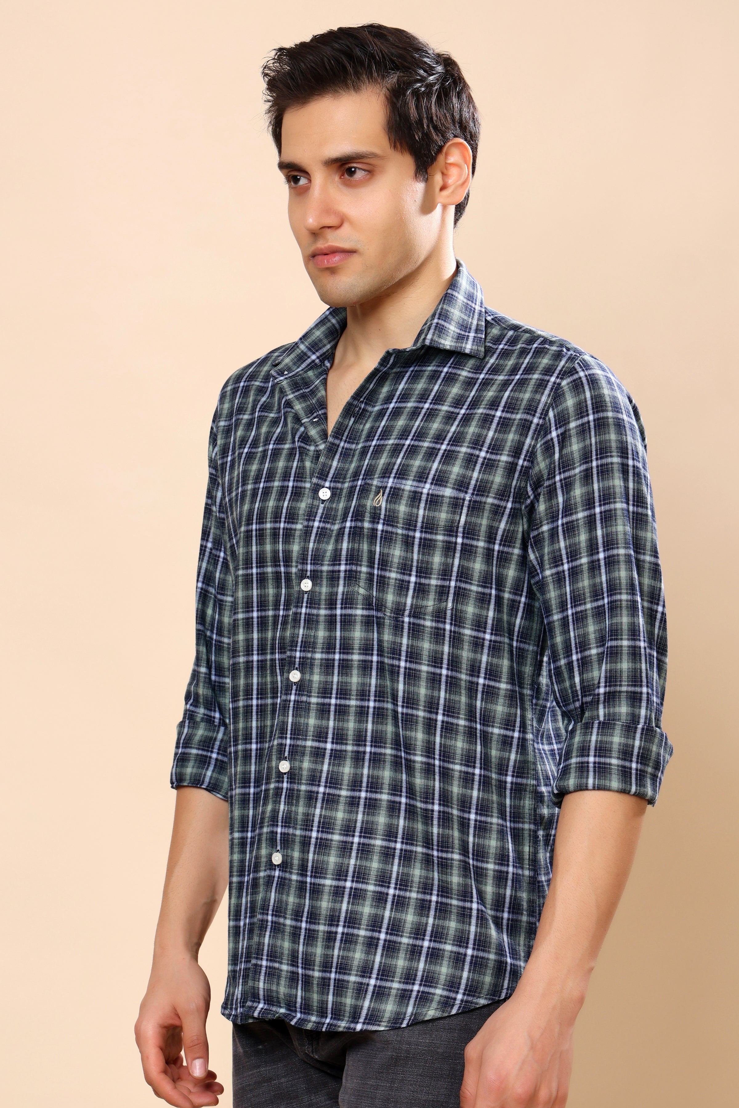 A man wearing a dark green and navy blue plaid button-down shirt with white lines, standing against a solid beige background.