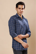 A man wearing a blue and white plaid long-sleeve button-up shirt, standing against a solid beige background.
