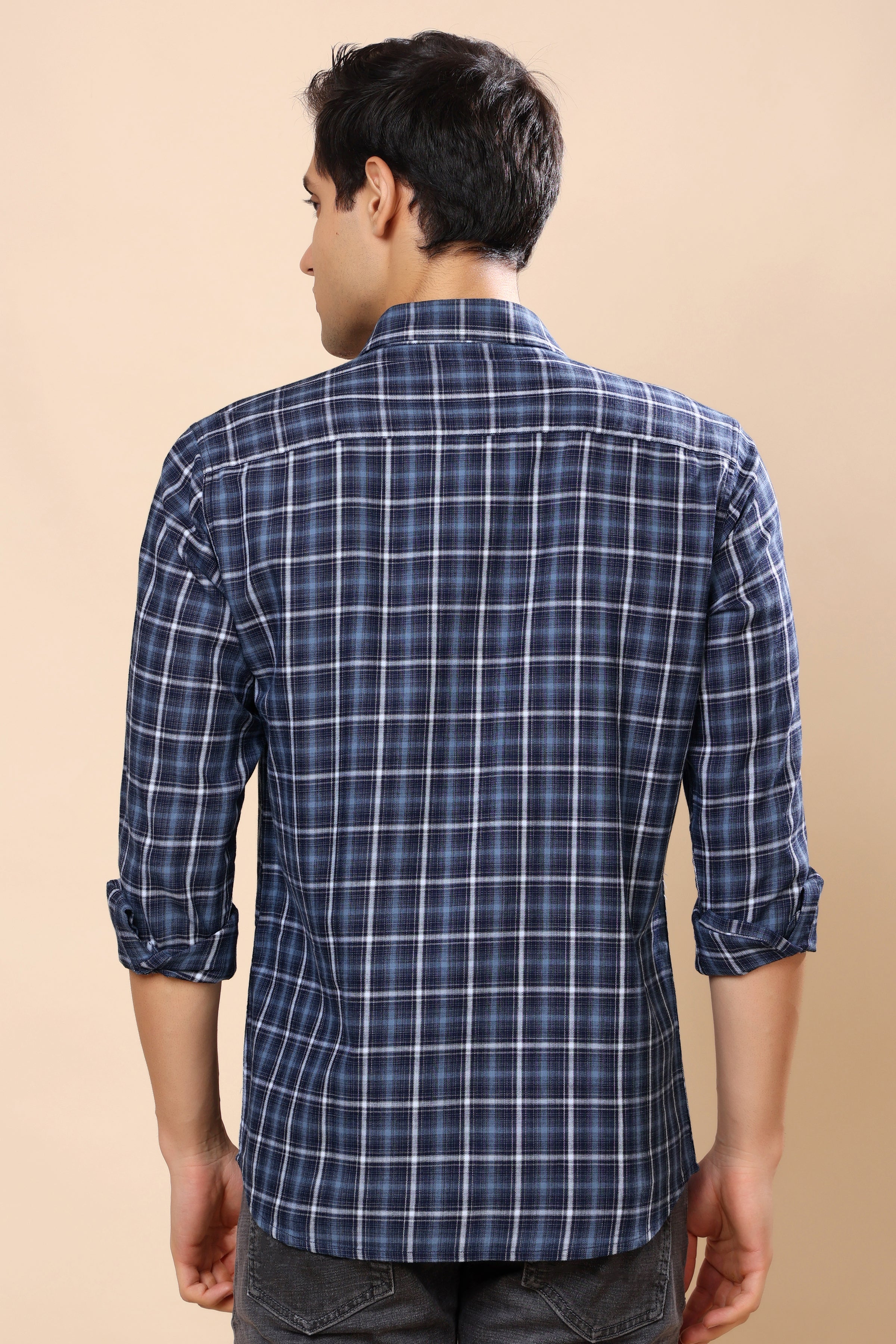 A man viewed from the back wearing a navy blue plaid long-sleeve shirt with white grid lines, set against a solid beige background.