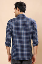 A man viewed from the back wearing a navy blue plaid long-sleeve shirt with white grid lines, set against a solid beige background.