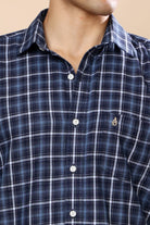 Close-up of a man wearing a navy blue plaid button-down shirt with white buttons and a small embroidered logo on the chest.